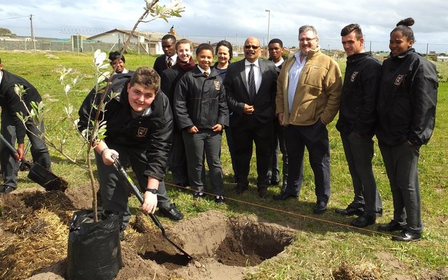 Marc John Hayes (Gr 11) van Gansbaai Academia is besig om ‘n boom te plant, met Riaan Conradie (AfriForum) 3de van regs en Tommy Wilson (skoolhoof) langs hom